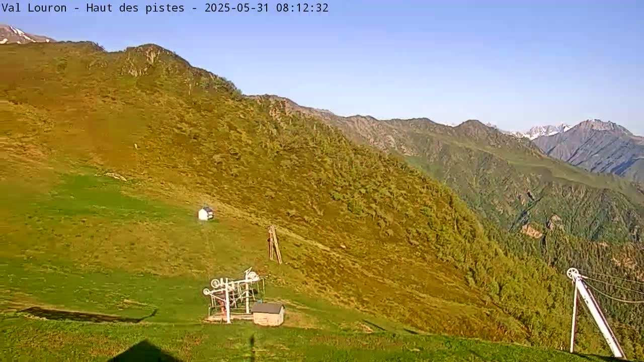 A mountainside with sparse vegetation, a small building, and a ski lift is visible under a clear blue sky.