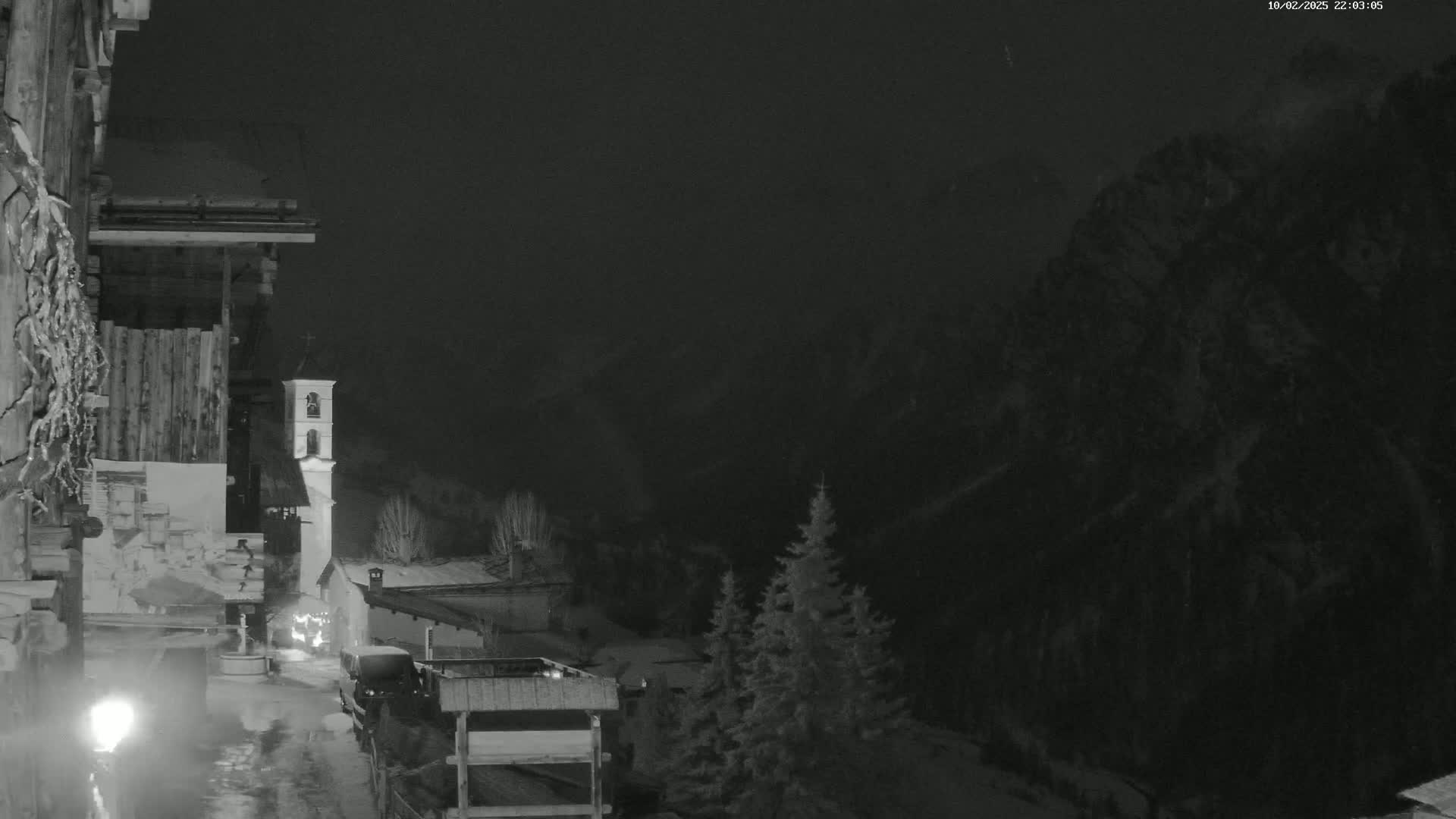 A nighttime, snowy scene shows a village nestled in a valley between dark mountains, with a church bell tower visible.