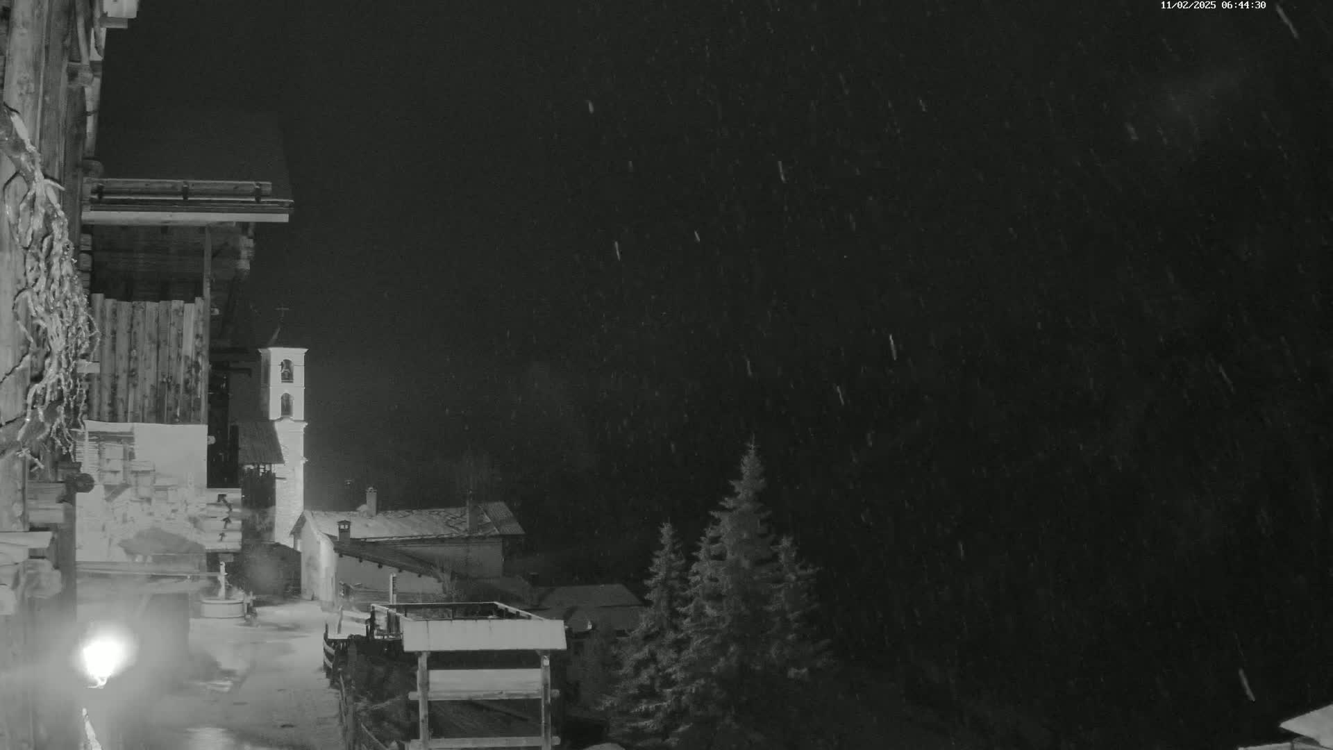 A nighttime view of a snow-covered village with a church steeple, under heavy snowfall.