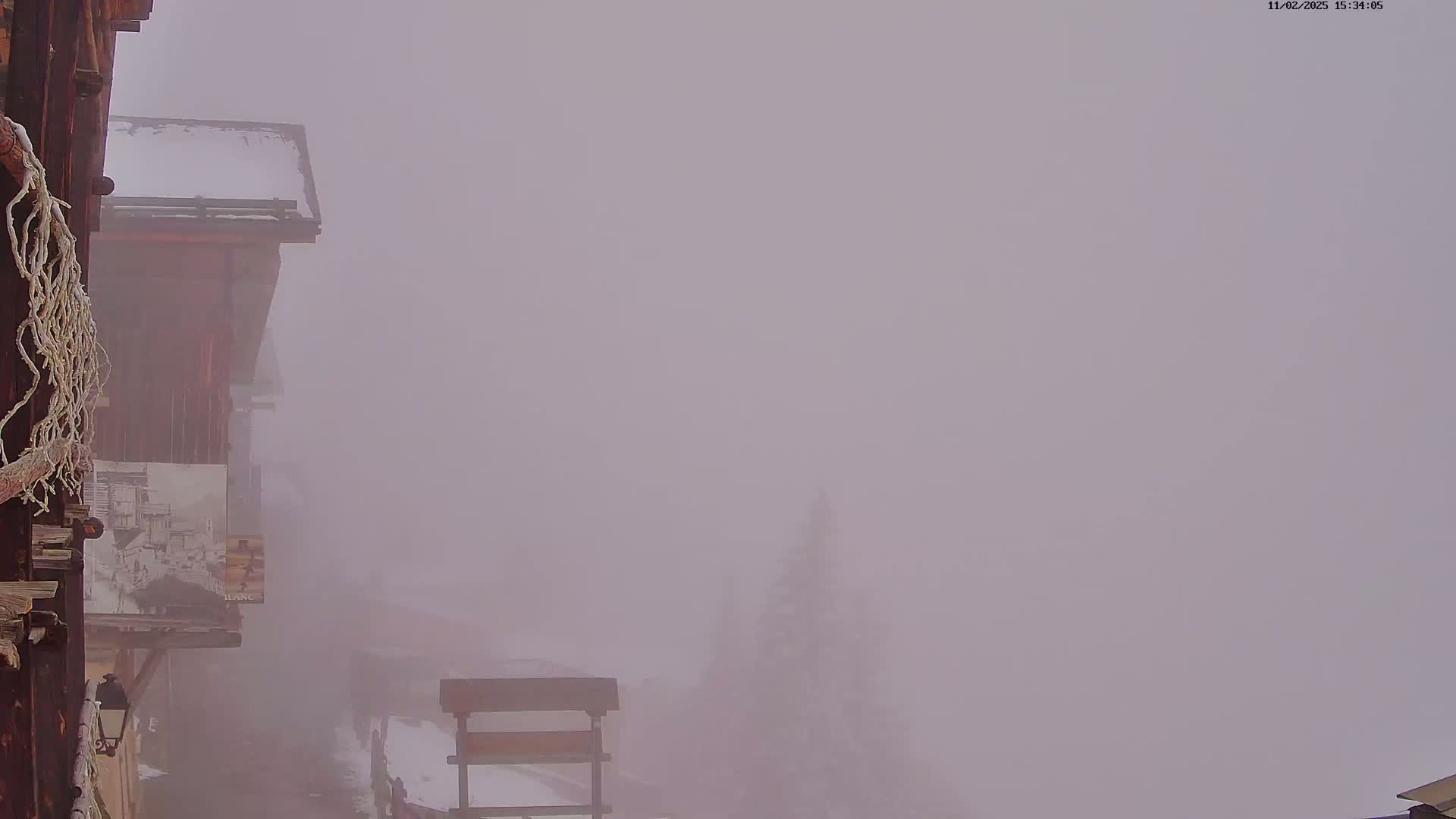 A snow-covered wooden building is partially visible through a thick fog.