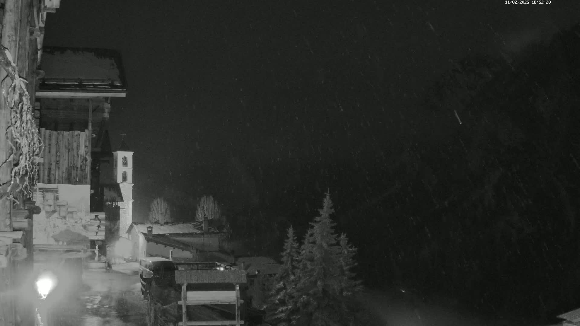 A nighttime snow scene shows a small village with a church bell tower, viewed from a snow-covered building.