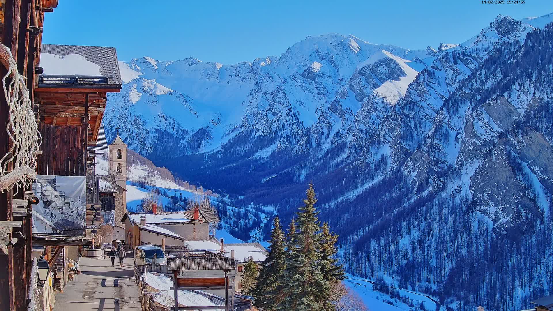 A snow-covered mountain village nestled in a valley, with a clear blue sky and snow-capped mountains in the background.