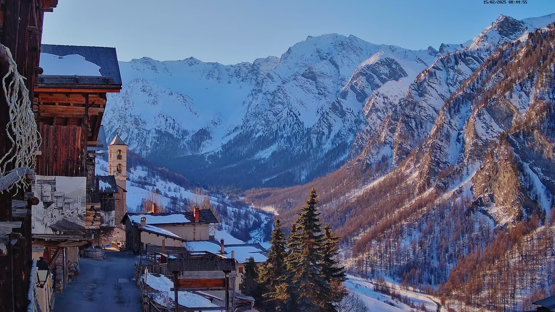 A snow-covered mountain village nestled in a valley between snow-capped mountains under a clear sky.