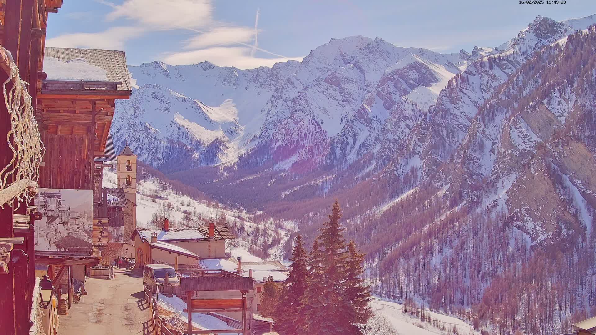 A snow-covered mountain village nestled in a valley surrounded by snow-capped mountains under a mostly sunny sky.
