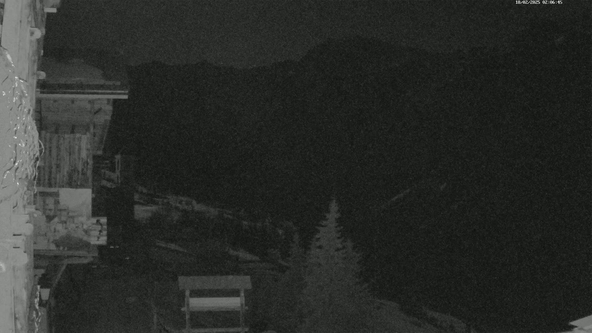 A nighttime, low-light image shows a portion of a wooden building with a dark mountainous landscape in the background.