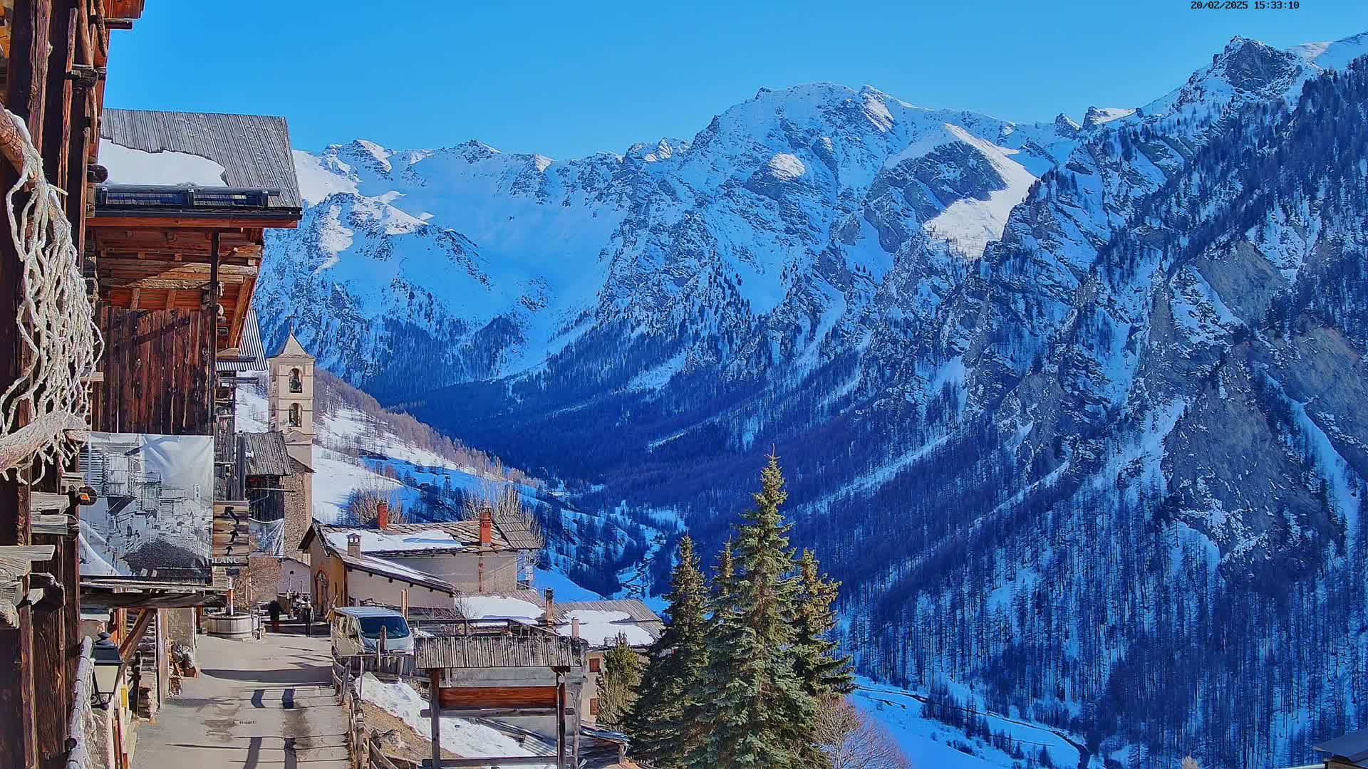 A snow-covered mountain village nestled in a valley between towering, snow-capped mountains under a clear blue sky.