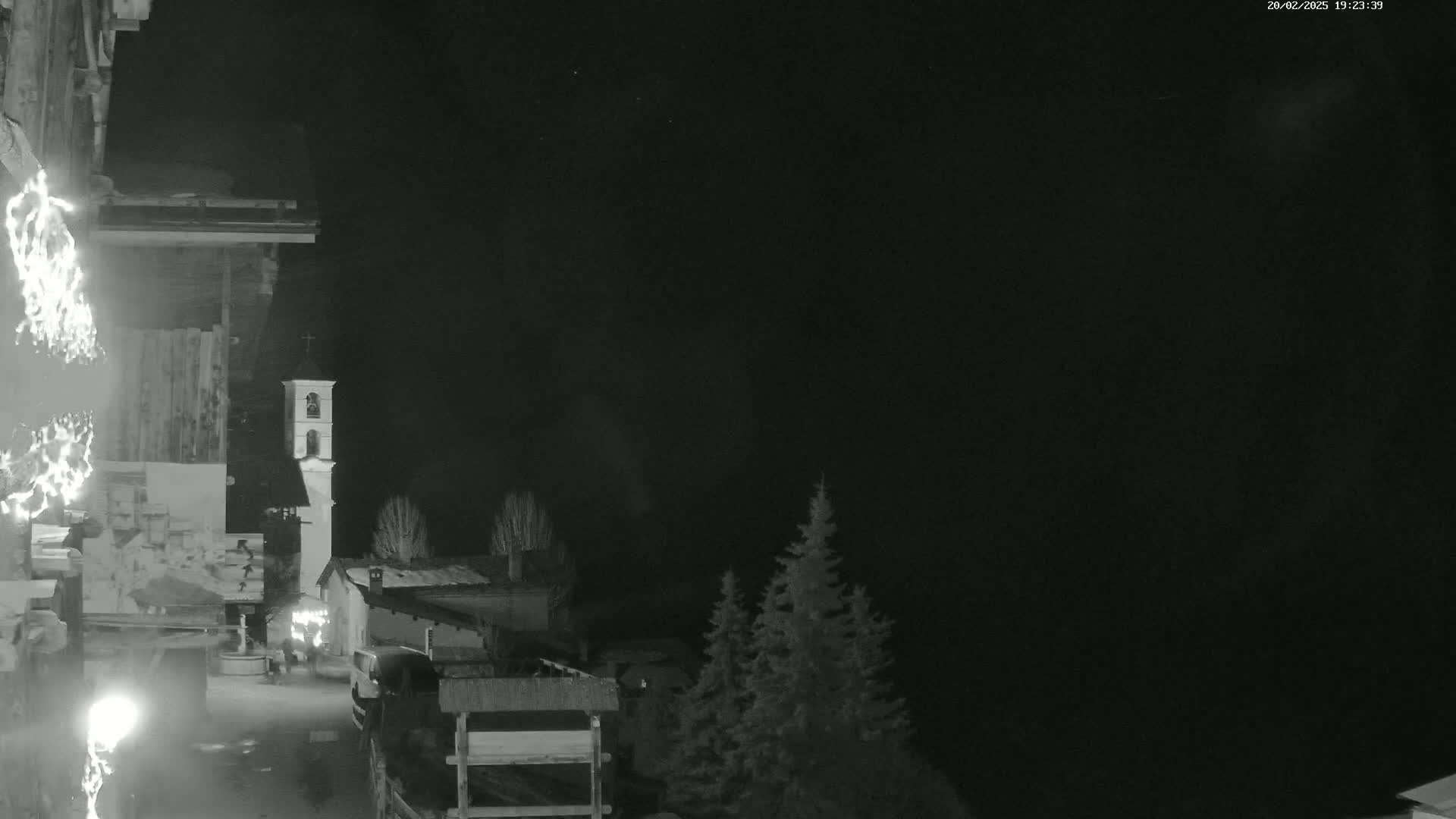 A nighttime, black-and-white view shows a small village with a bell tower under a clear, dark sky.