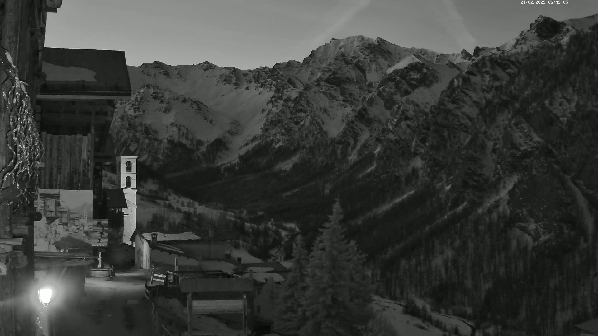 A snow-covered mountain range is visible behind a small village at night, lit by a single lamppost.