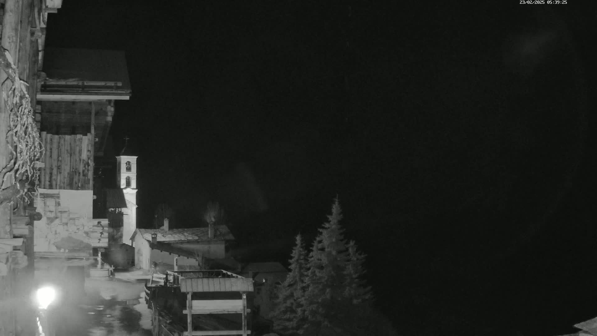 A nighttime, black-and-white view of a village with a church steeple, illuminated by a single light source, under a dark sky.