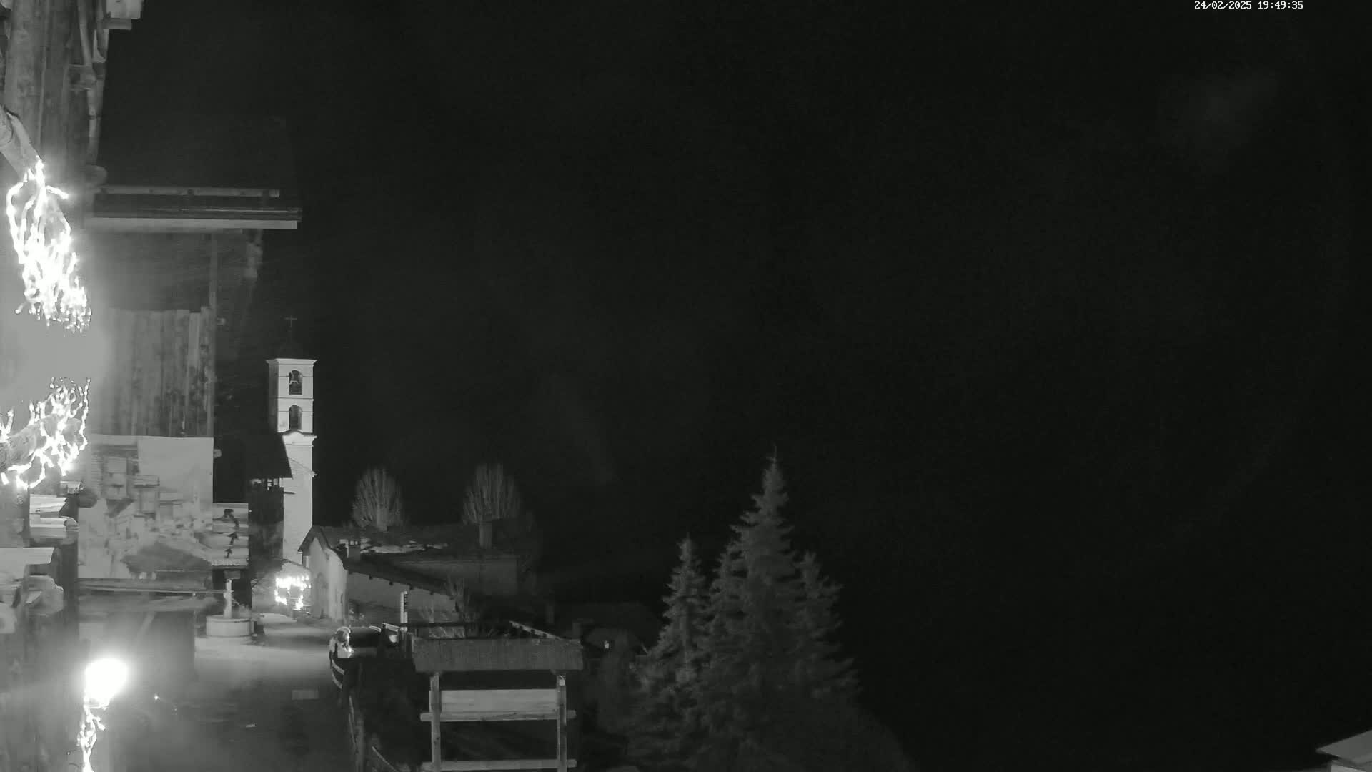 A nighttime view of a village scene, featuring a bell tower and some trees under a dark sky.