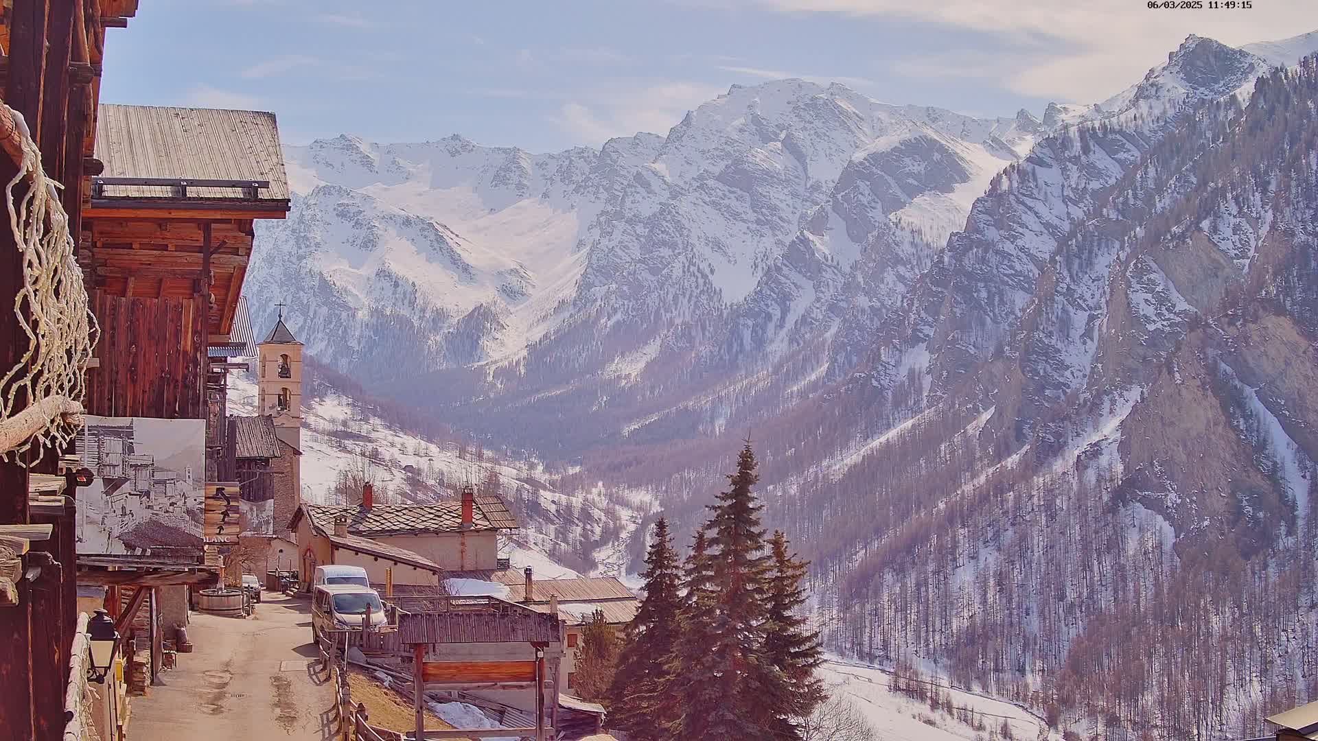 A small village nestled in a valley, surrounded by snow-covered mountains under a clear blue sky.