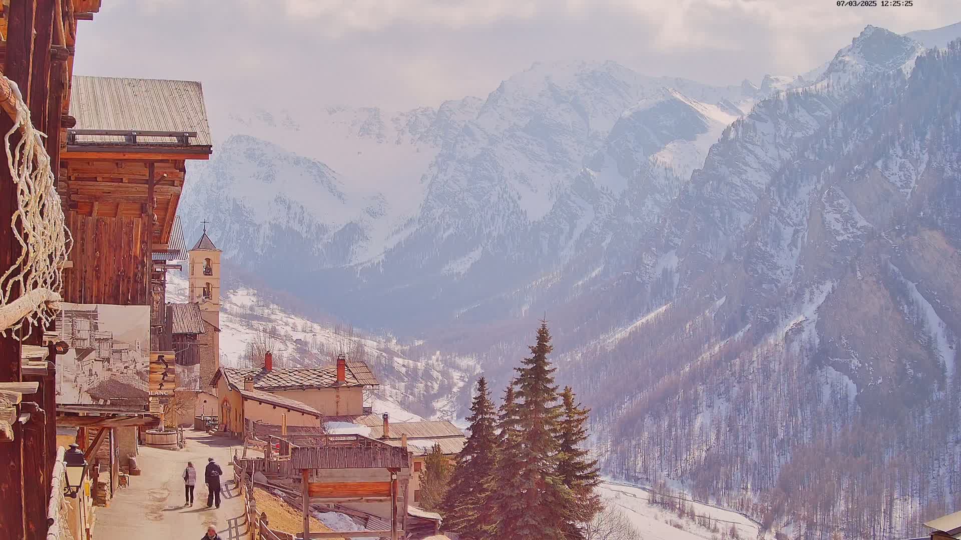 A quaint village nestled in a snow-covered mountain valley under a partly cloudy sky.