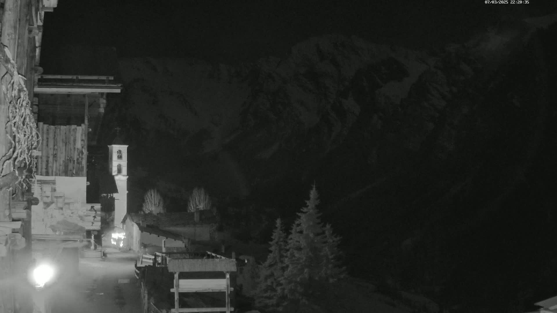 A nighttime view of a village nestled in a snow-covered mountain valley under a dark sky.