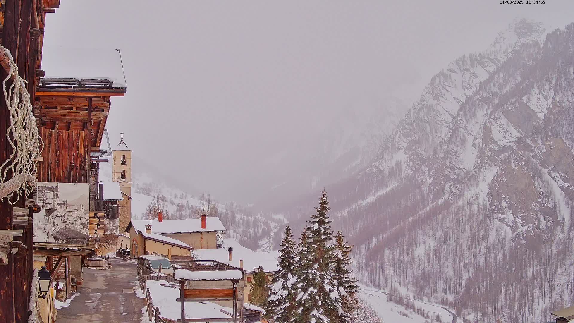 A snow-covered village nestled in a valley between snow-dusted mountains under a hazy sky.