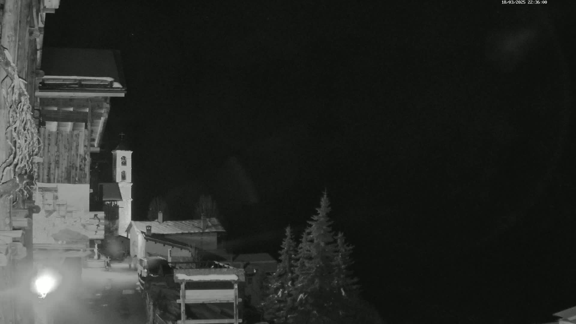 A nighttime, snow-covered village scene features a church steeple and other buildings under a dark sky.
