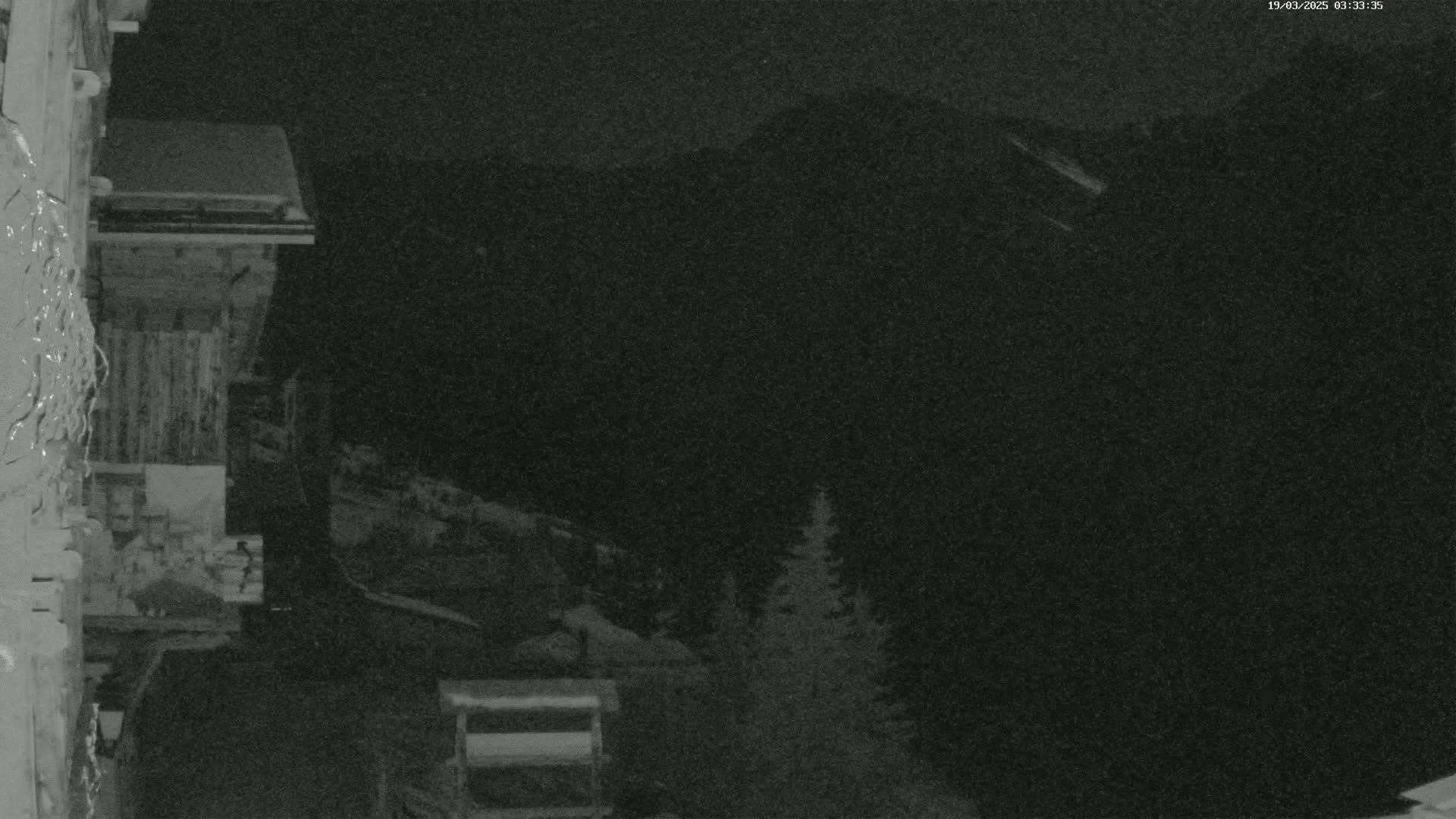 A nighttime view from a snow-covered building shows dark mountains in the distance under a clear, dark sky.