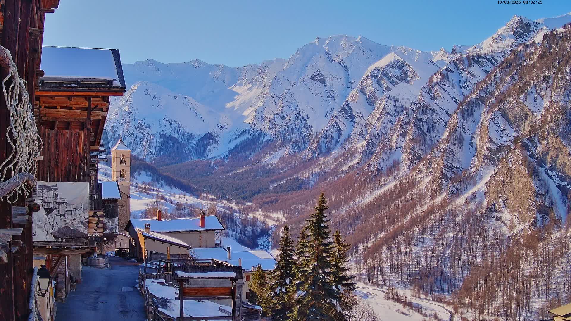 A snow-covered village nestled in a valley, surrounded by snow-capped mountains under a clear blue sky.