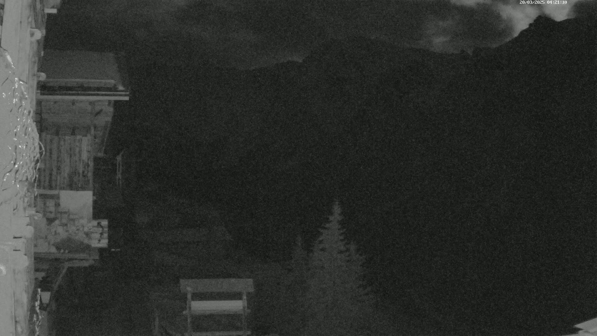 A nighttime view shows a snow-covered wooden structure and a dark mountain range under a cloudy sky.