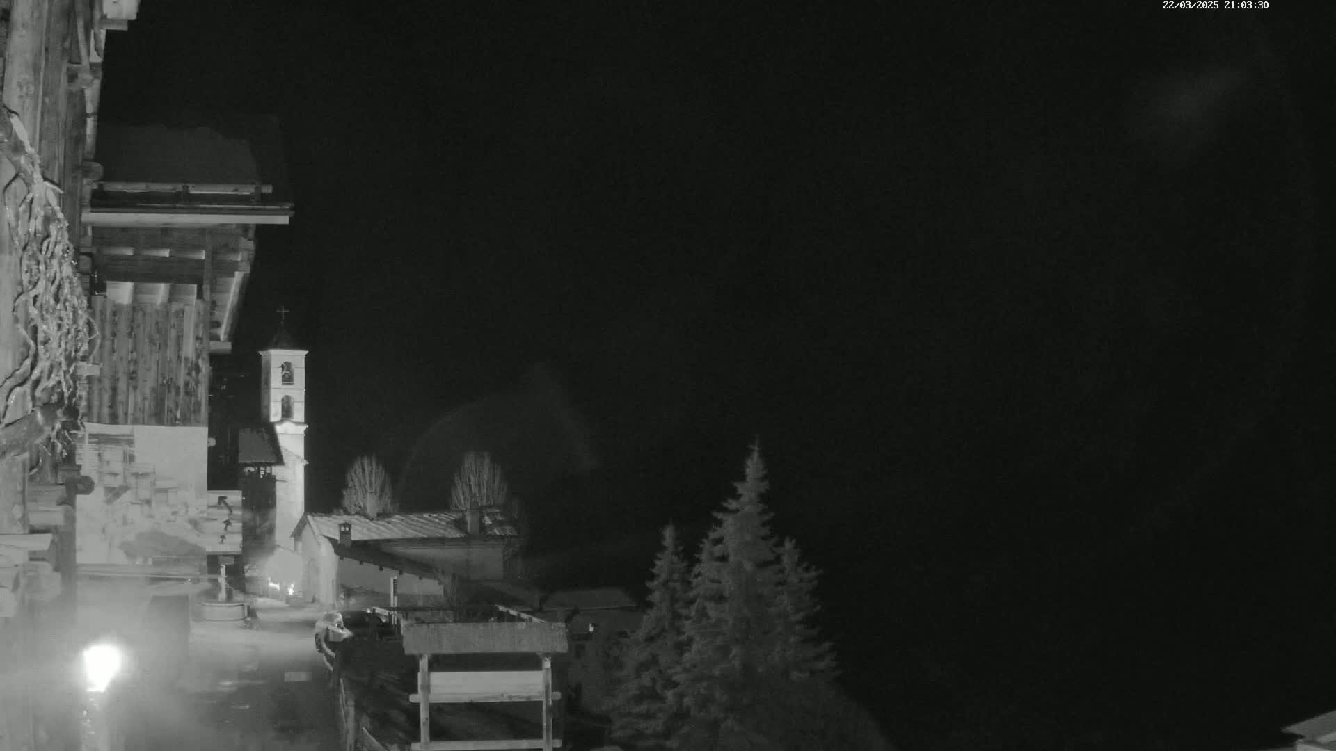 A nighttime, snow-covered village scene shows a church steeple and buildings under a dark sky.