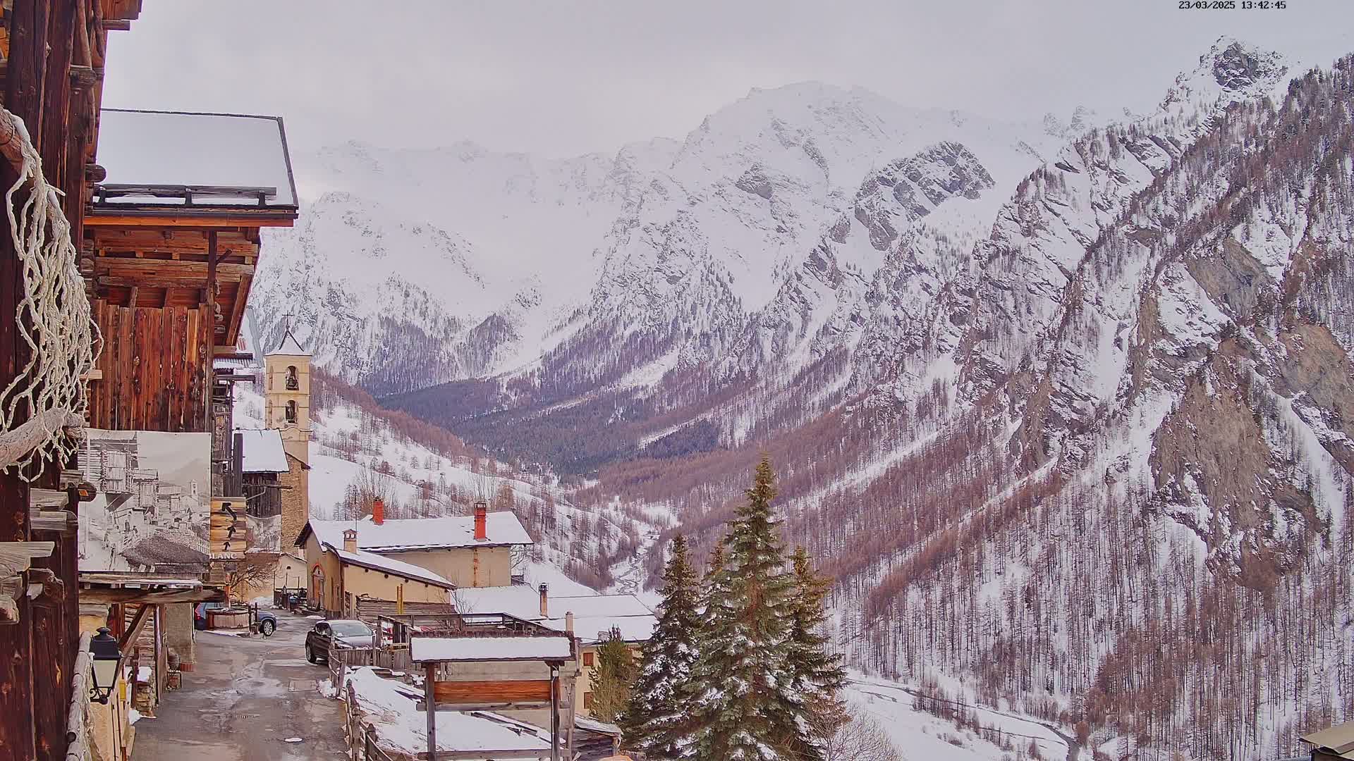 A snow-covered village nestled in a valley between towering snow-capped mountains on an overcast day.