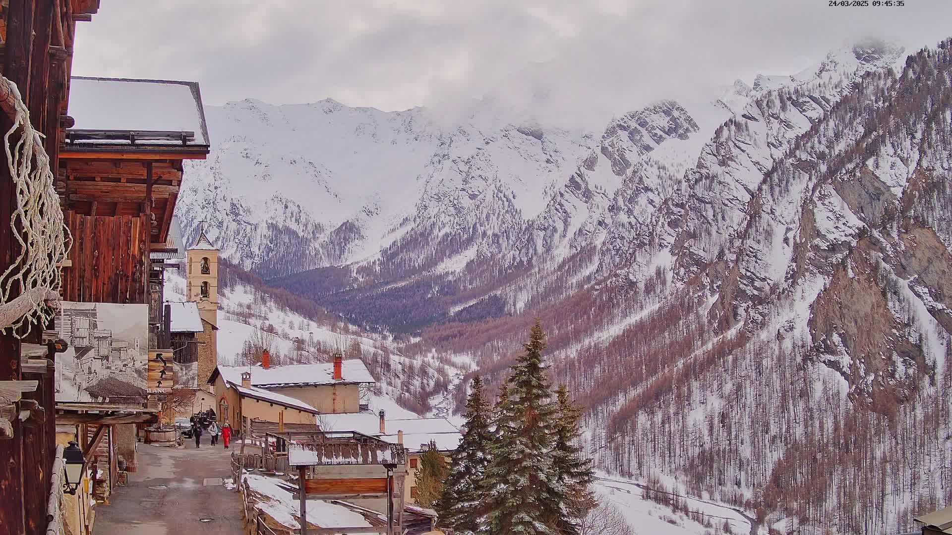A snow-covered village nestled in a valley between snow-capped mountains under an overcast sky.