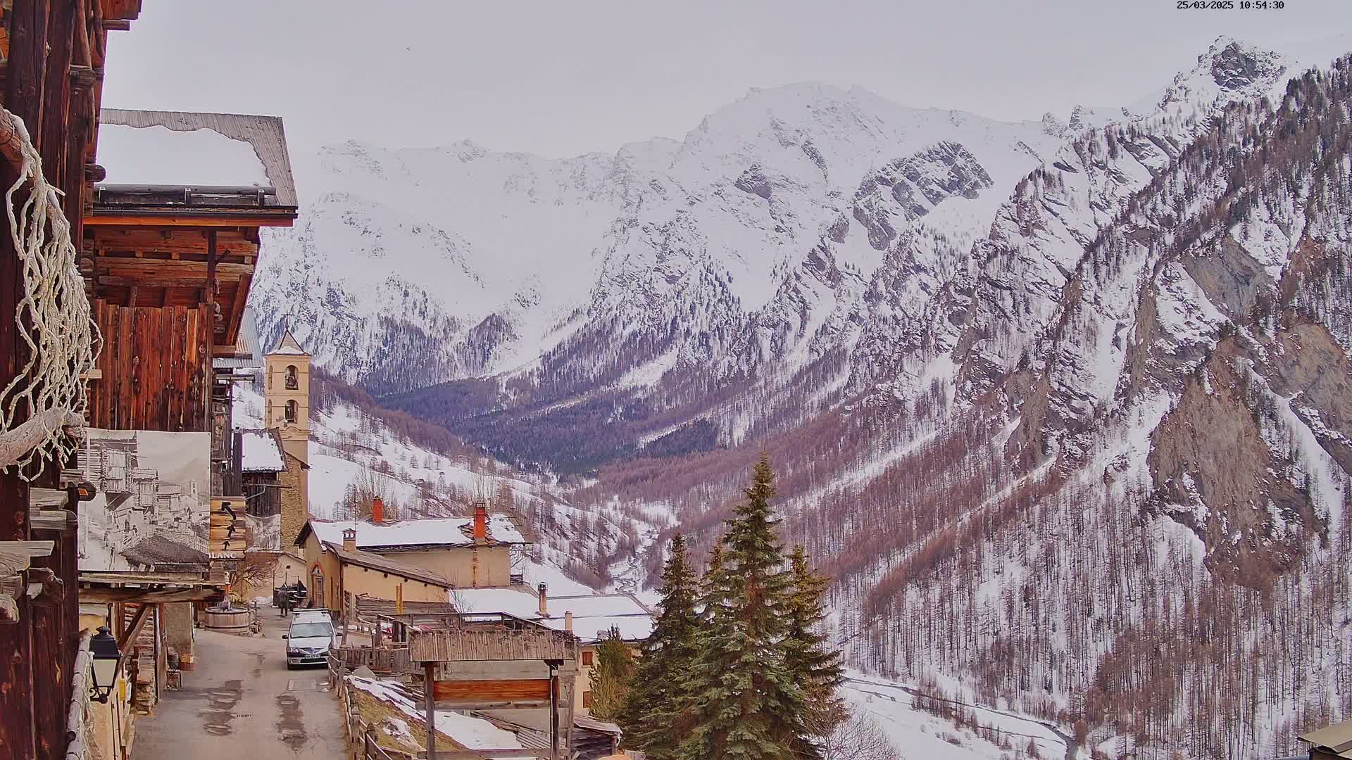 A snow-covered village nestled in a valley between towering, snow-capped mountains on an overcast day.