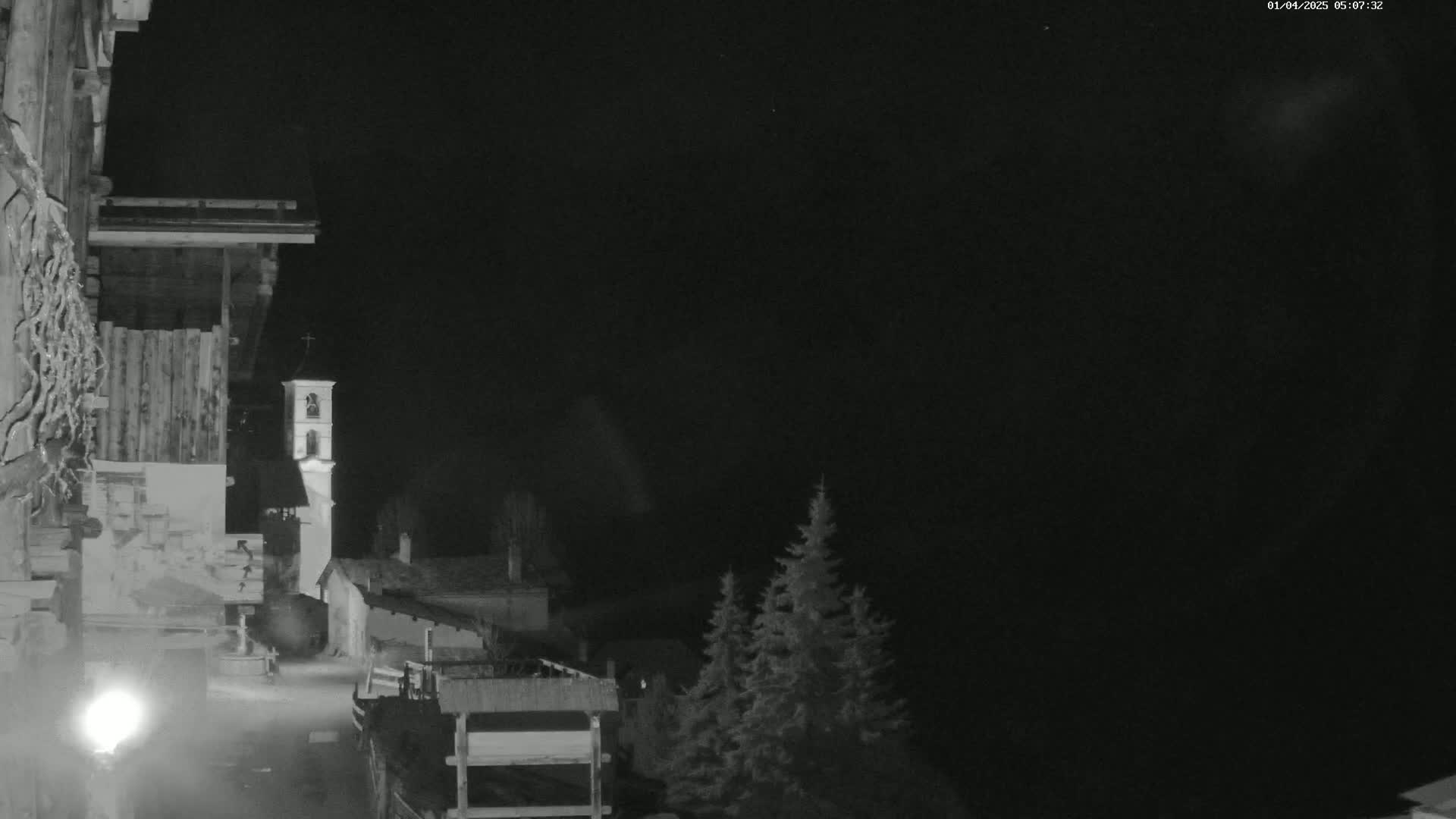 A nighttime, black-and-white view of a village with a church steeple, seen from a building's exterior, under a clear, dark sky.