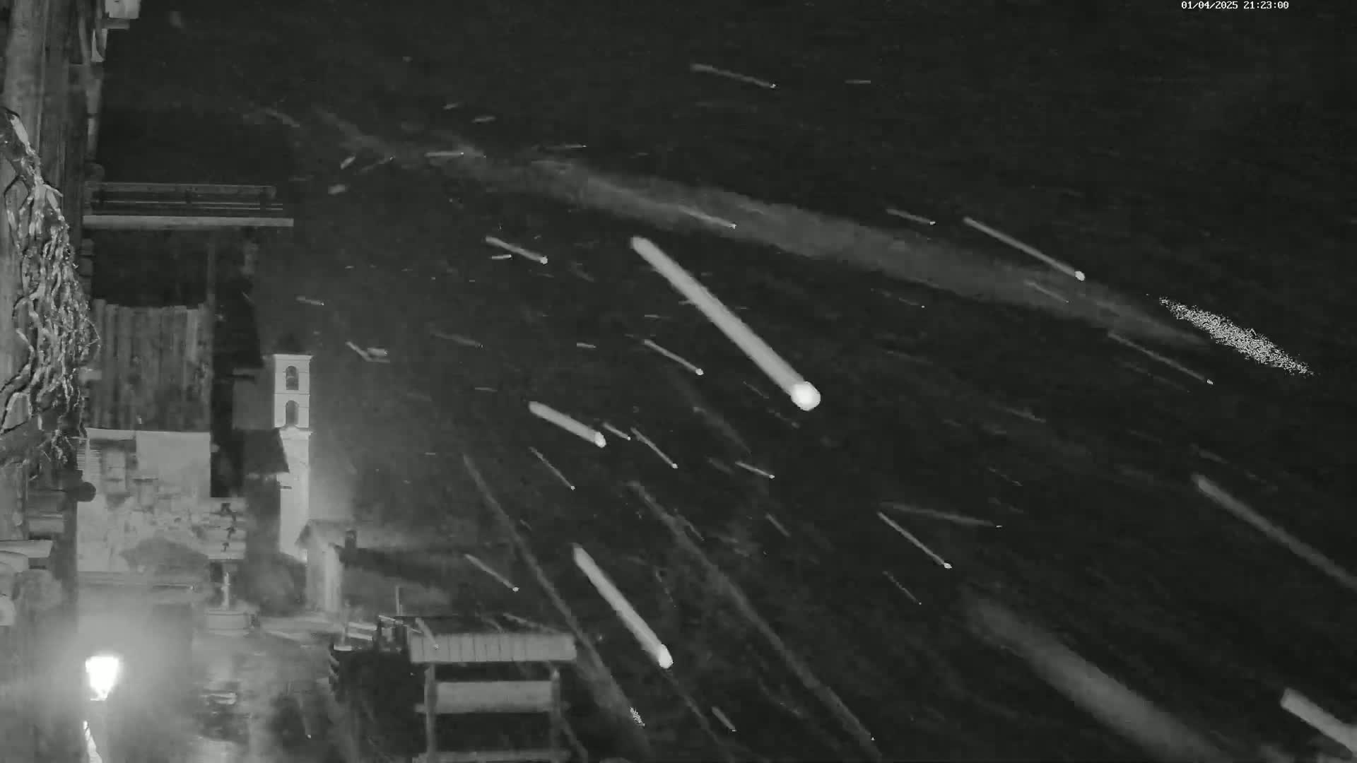 A nighttime, snowy scene shows numerous bright streaks of light falling across a dark sky above a village with buildings and a streetlight.