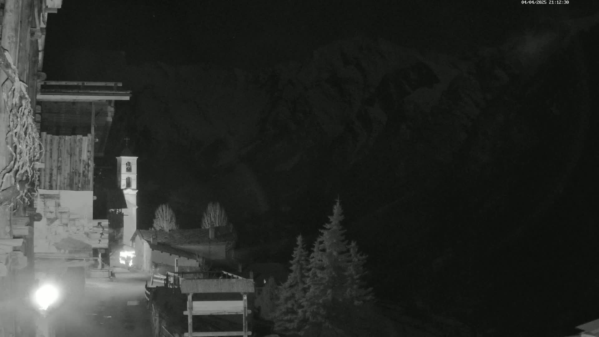 A nighttime, black-and-white view of a small village nestled against a mountain range under a dark sky.