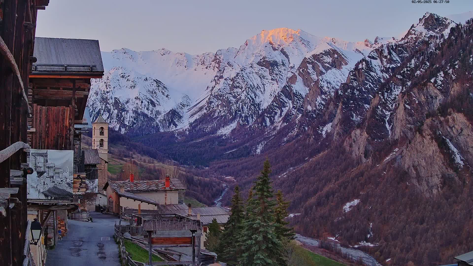 A mountain village nestled in a valley, with snow-capped mountains in the background under a twilight sky.