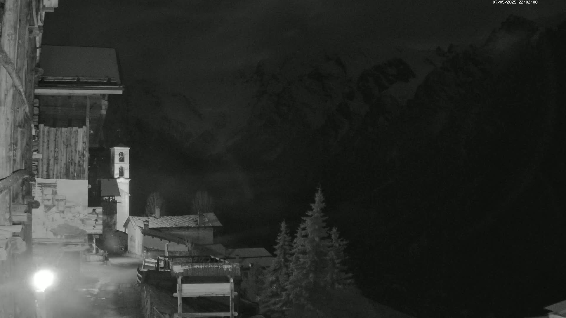 A nighttime view of a snow-covered village nestled in a dark mountain valley under a cloudy sky.