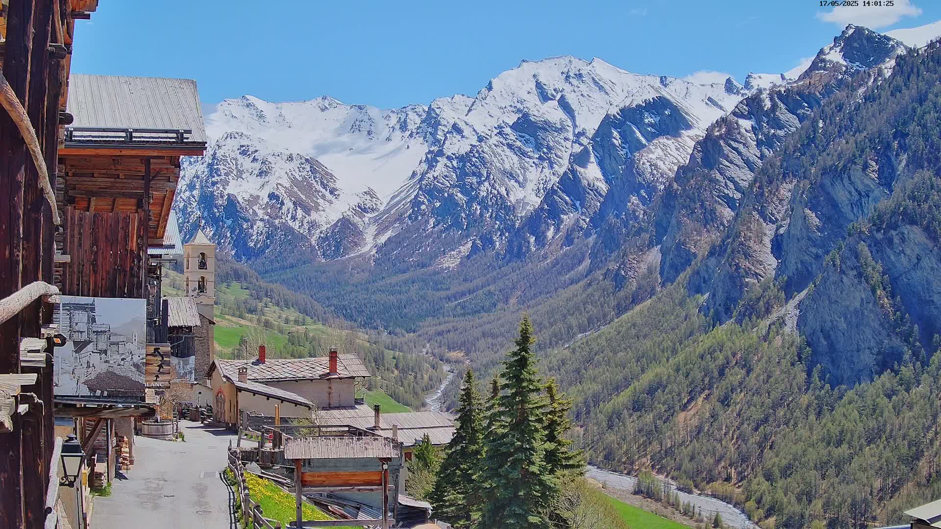 A mountain village nestled in a valley, overlooked by snow-capped mountains under a clear blue sky.