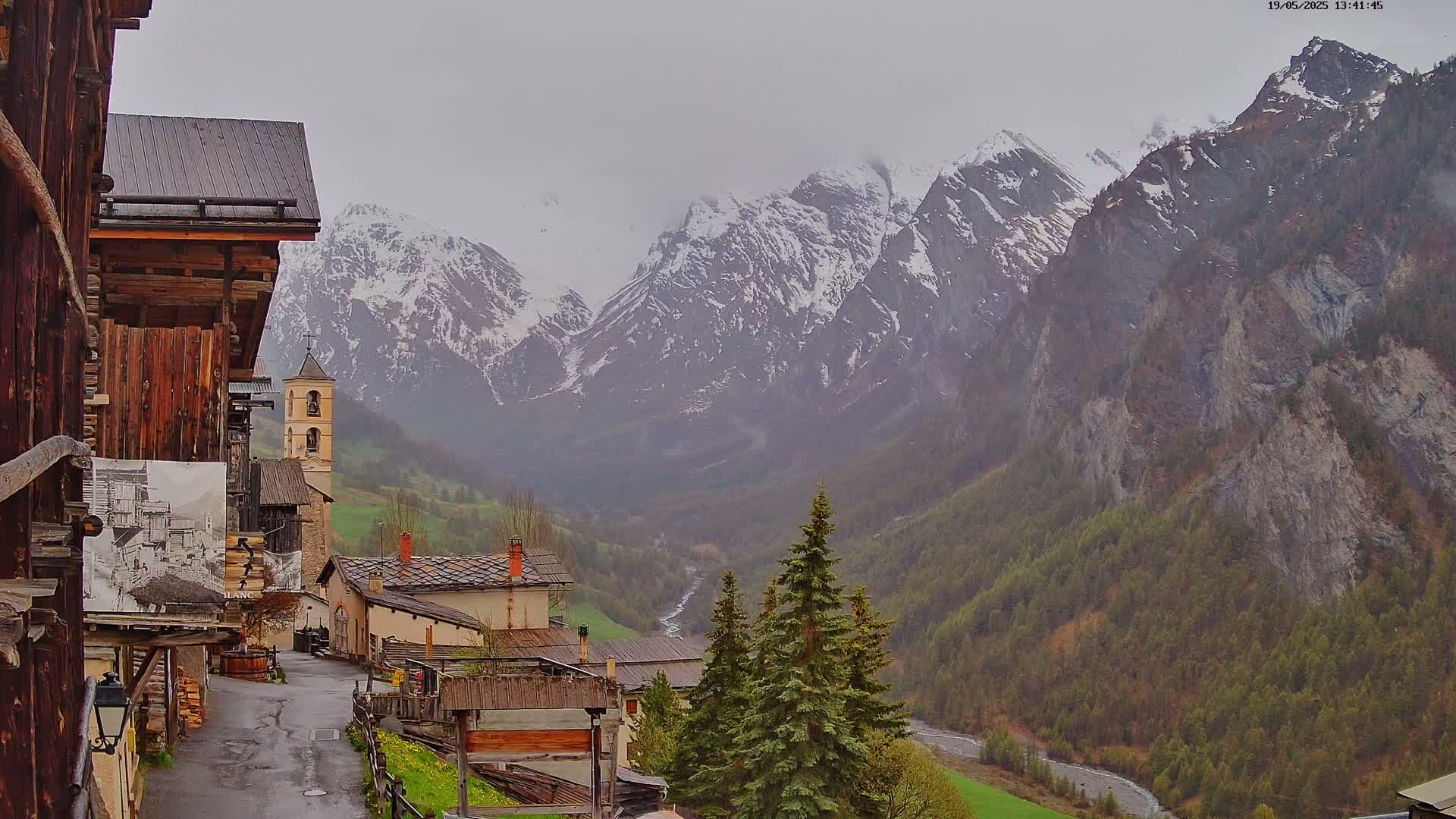 A view of a small village nestled in a valley between snow-capped mountains on an overcast day.