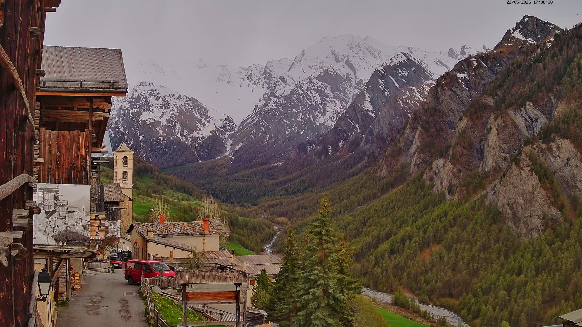 A mountain village nestled in a valley, with snow-capped mountains in the background under an overcast sky.