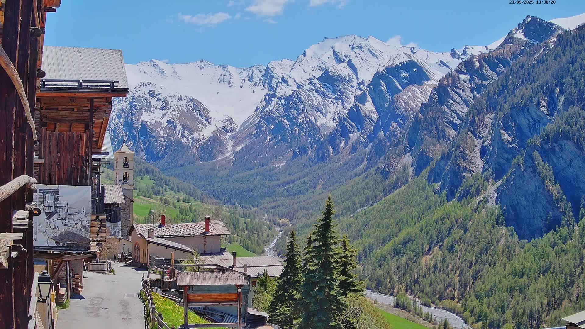 A quaint village nestled in a valley, surrounded by snow-capped mountains under a sunny sky.