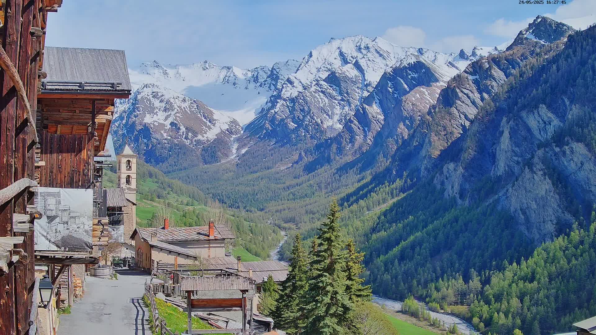 A quaint village nestled in a valley, surrounded by snow-capped mountains under a sunny sky.