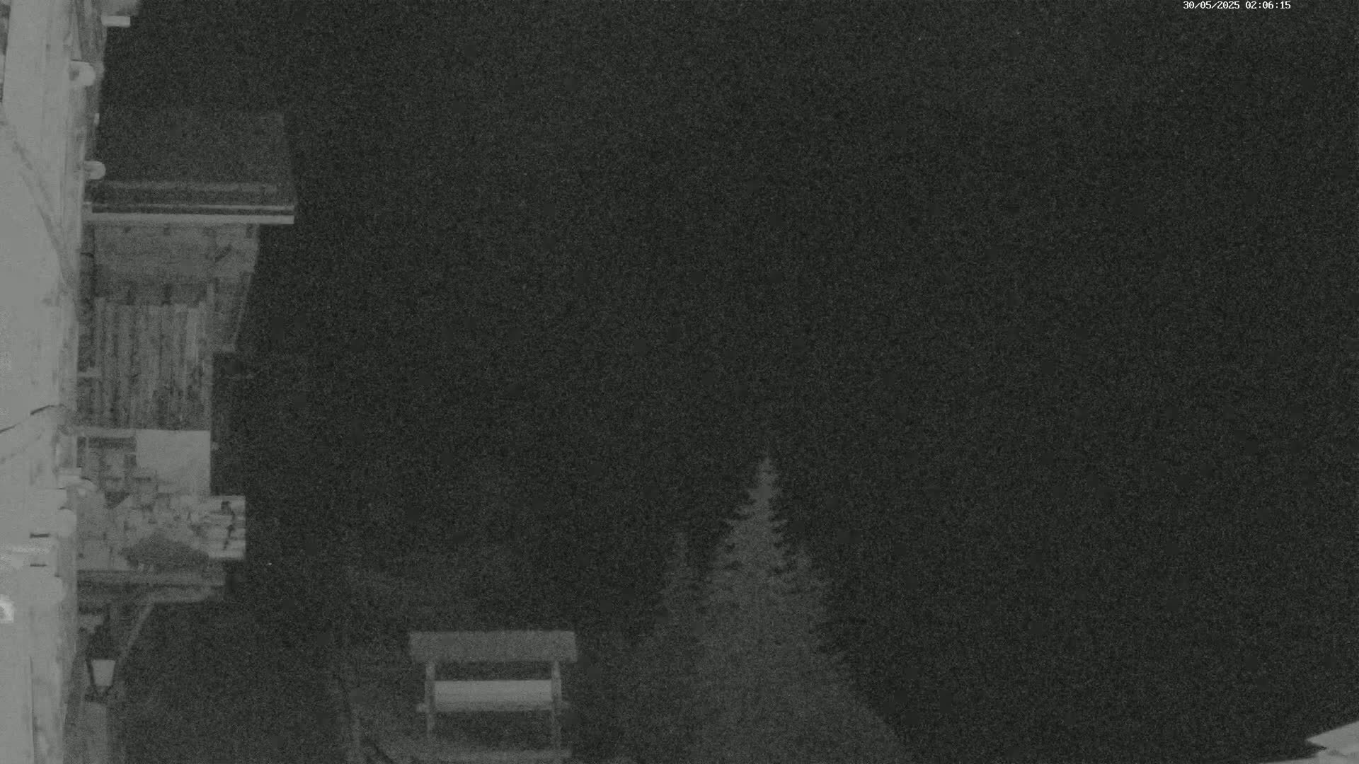 A nighttime, low-light image shows a section of a building's exterior, with some trees visible in the background under a dark sky.