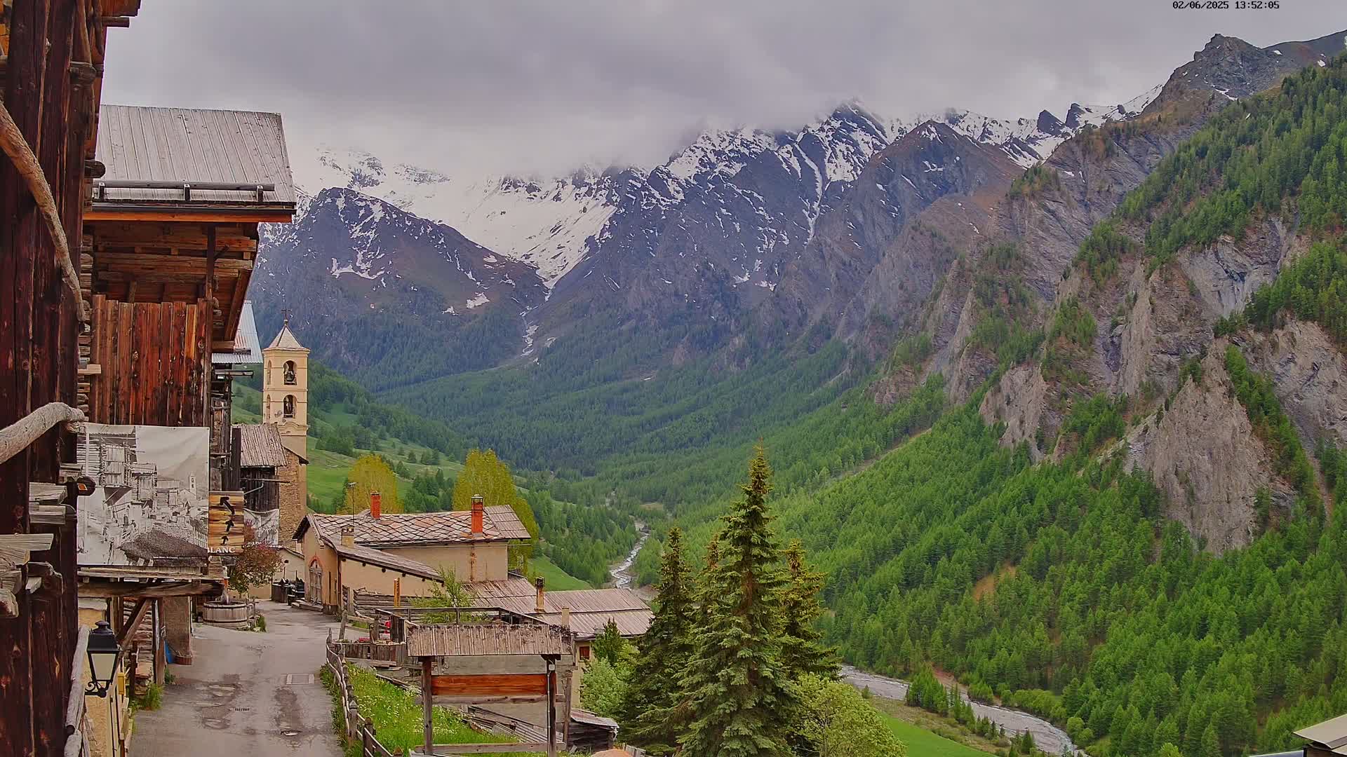 A quaint village nestled in a valley, overlooked by snow-capped mountains under a cloudy sky.