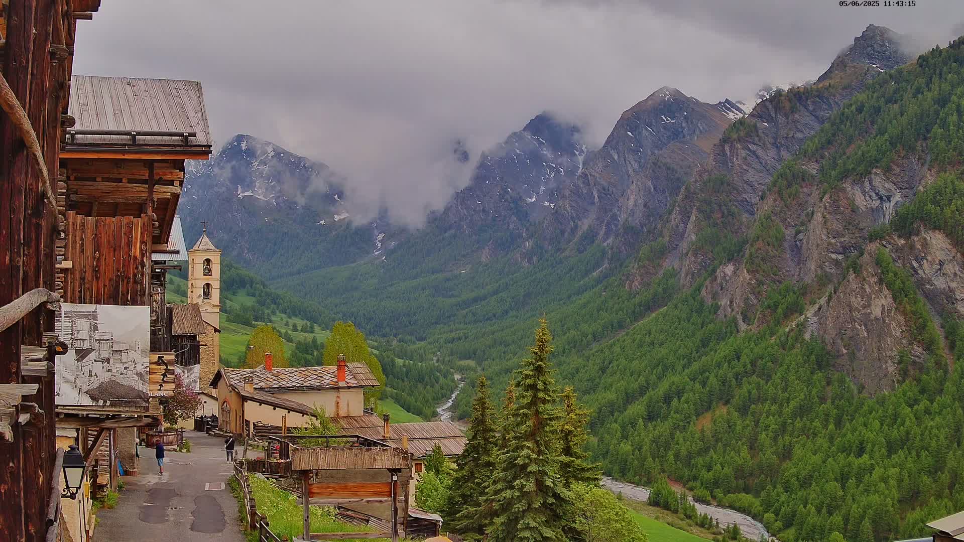 A small village nestled in a valley between towering, cloud-covered mountains on an overcast day.