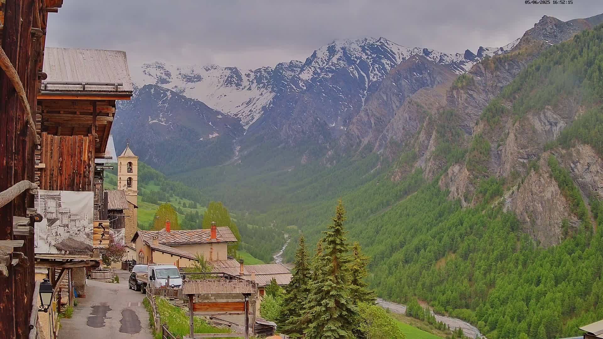 A mountain village nestled in a valley, with snow-capped mountains in the background under an overcast sky.