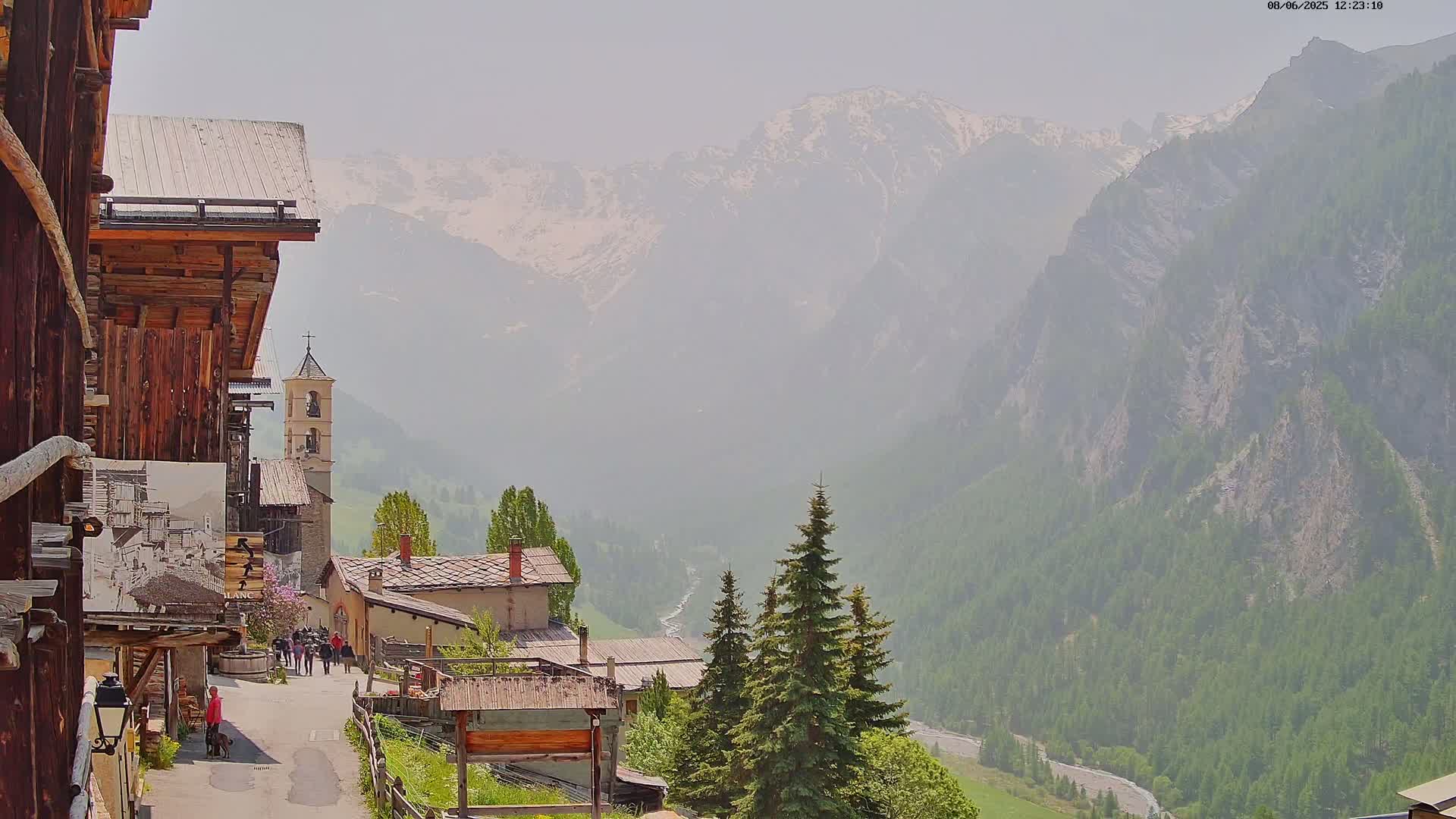 A hazy view of a mountain village nestled in a valley, with snow-capped mountains in the background.
