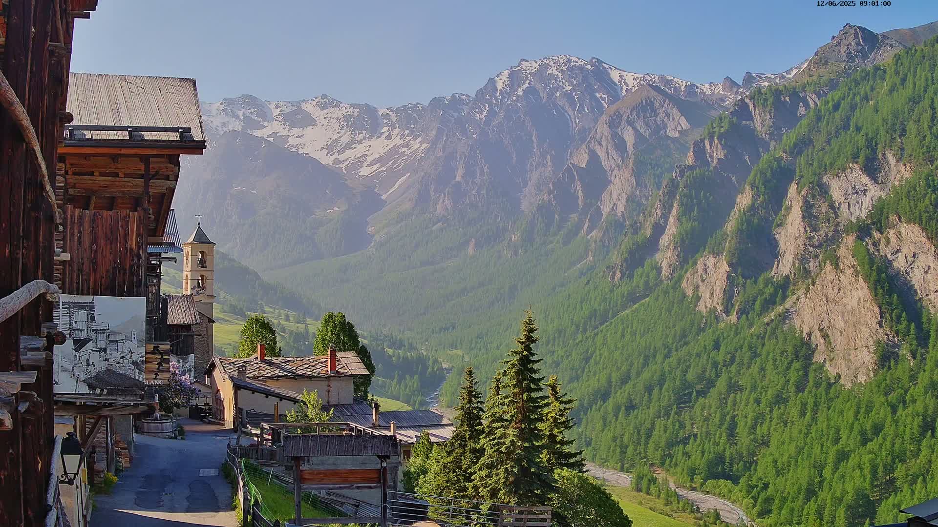 A quaint village nestled in a valley, overlooked by snow-capped mountains under a clear, sunny sky.