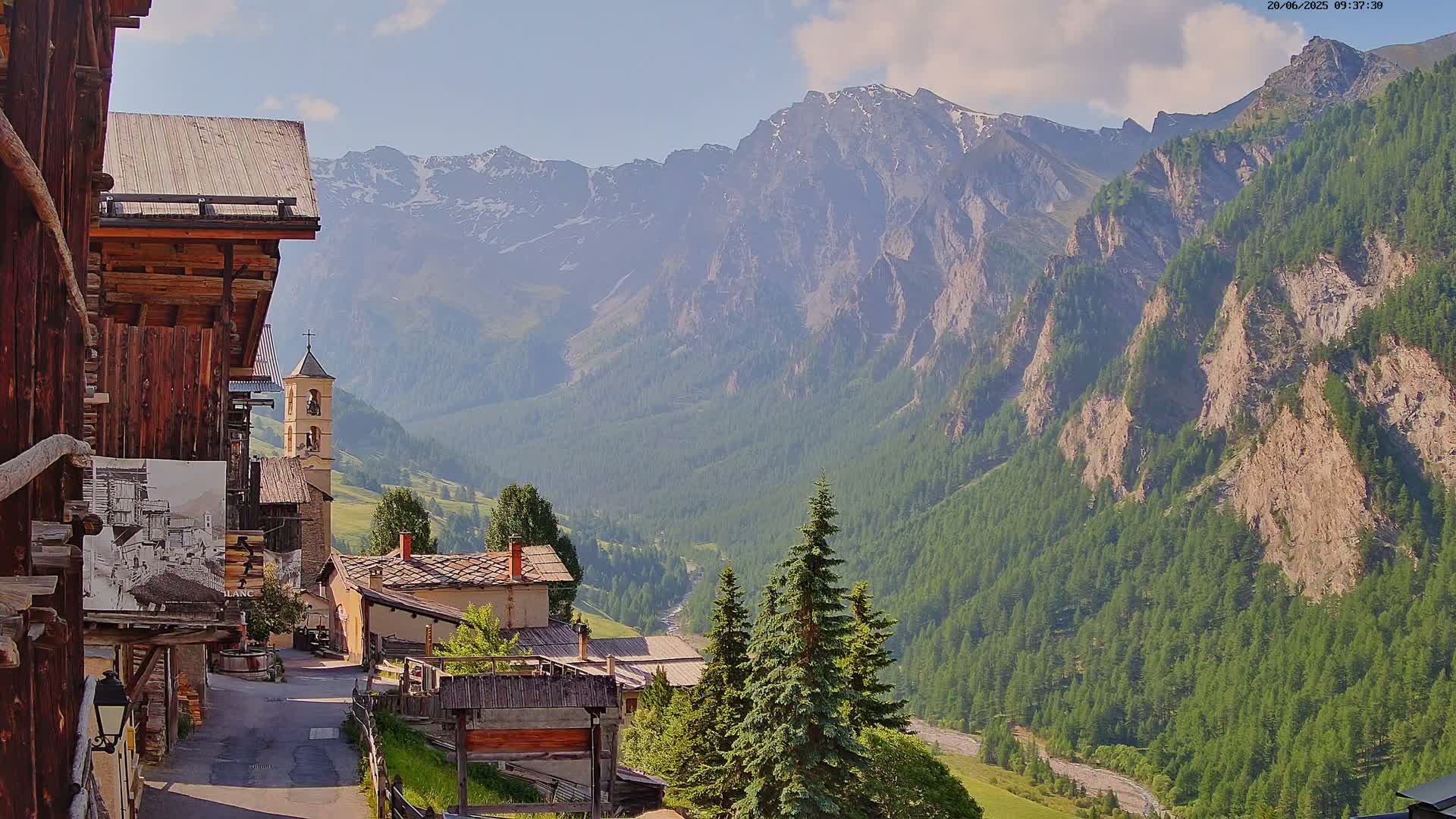 A quaint village nestled in a valley, surrounded by majestic mountains under a partly cloudy sky.