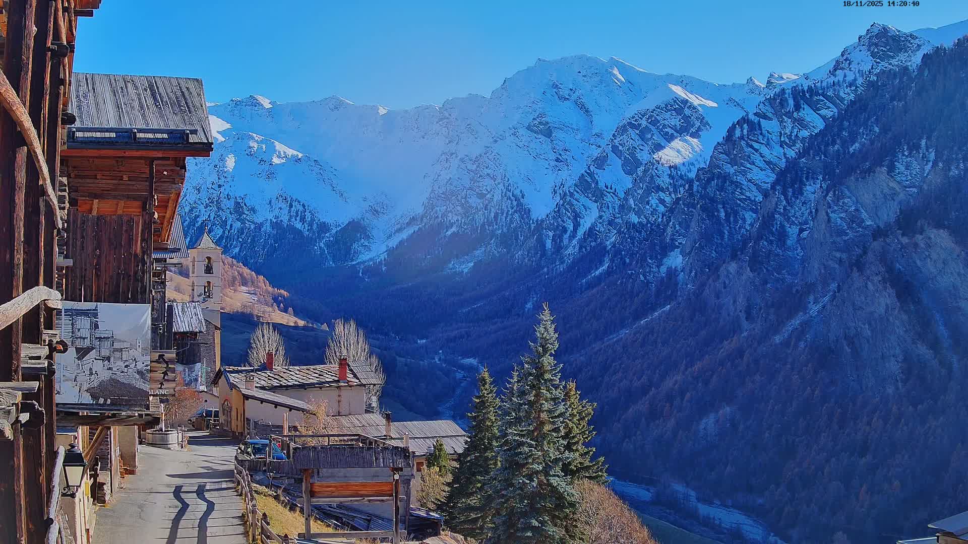 A nighttime view of a small village nestled in a valley, illuminated by a single lamppost, with a church steeple visible and dark, cloudy skies above mountains in the background.