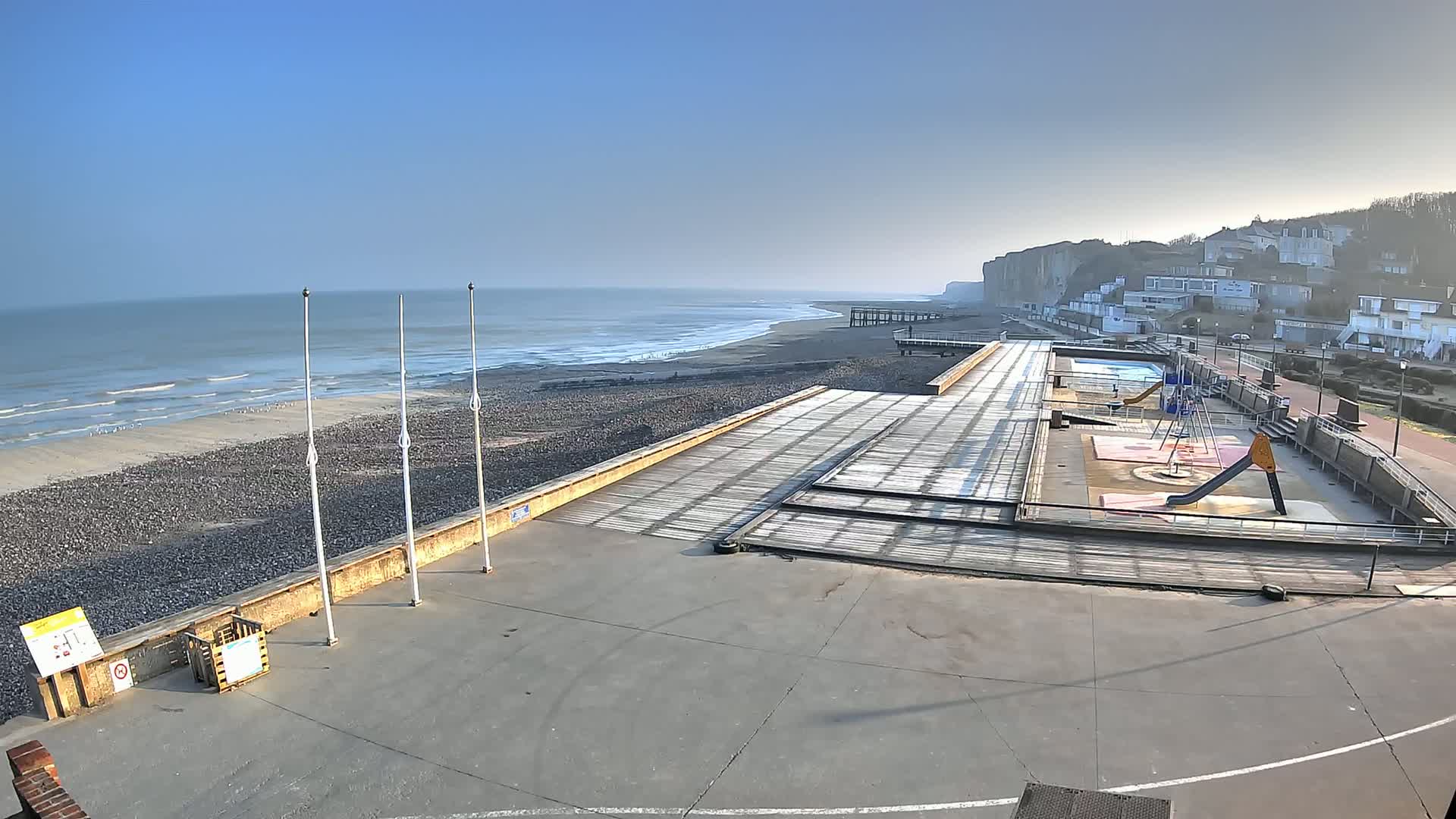A seaside promenade with a playground and a view of a calm ocean under a clear blue sky.