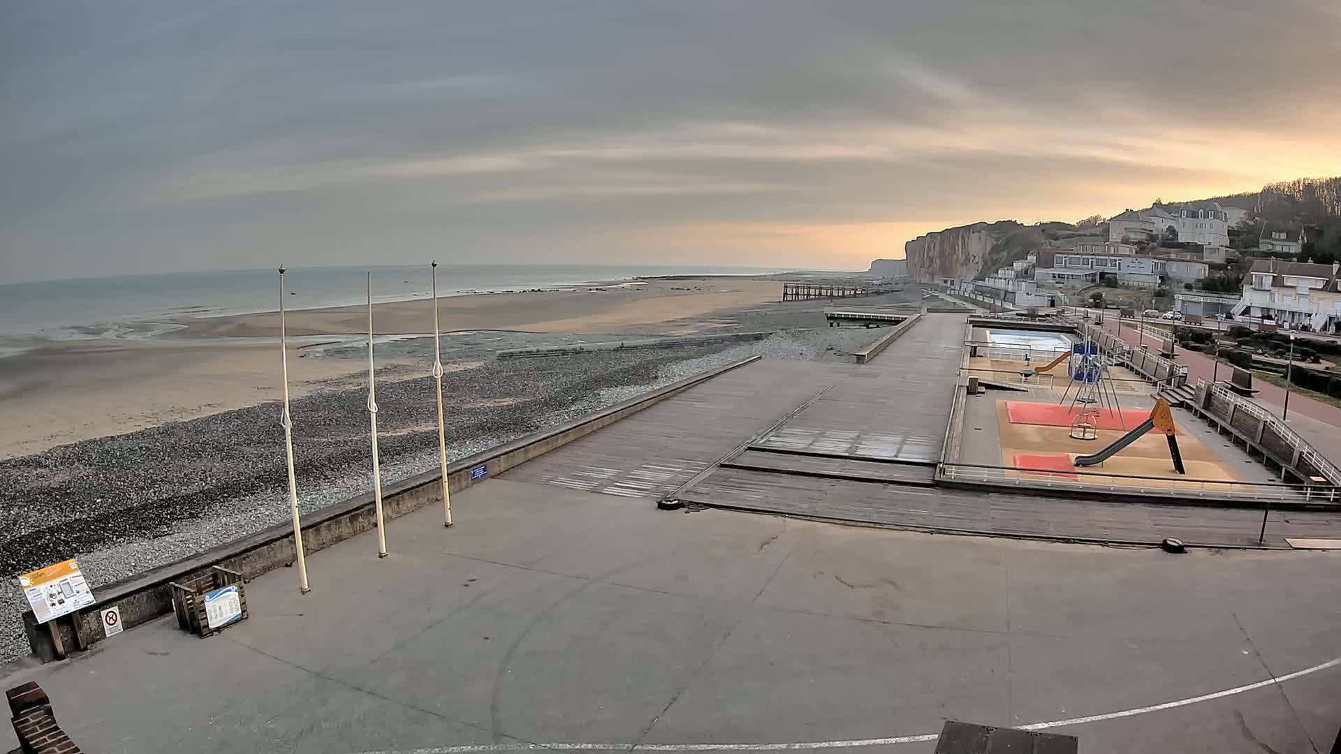 A seaside playground and boardwalk overlook a beach and chalk cliffs under an overcast sky.