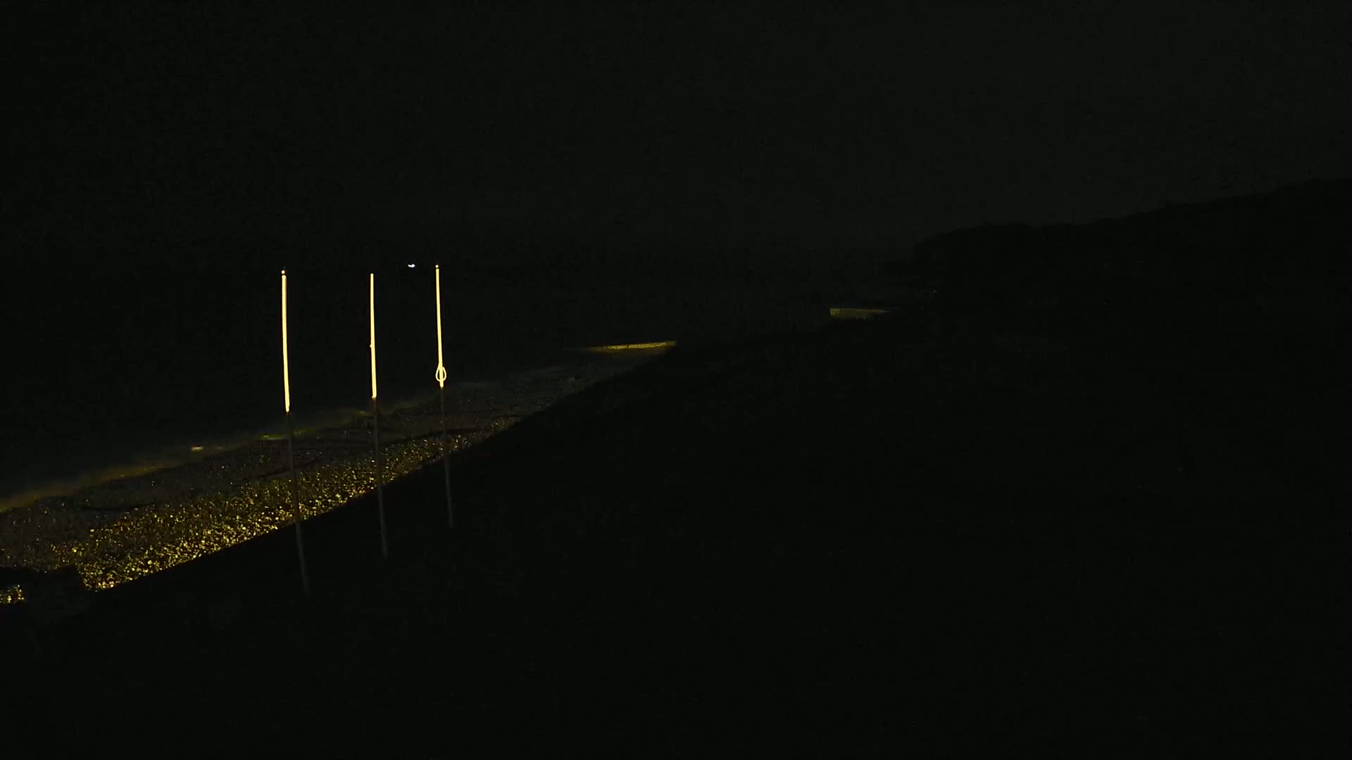 Three tall, slender lights illuminate a dark, glittering expanse of water at night.