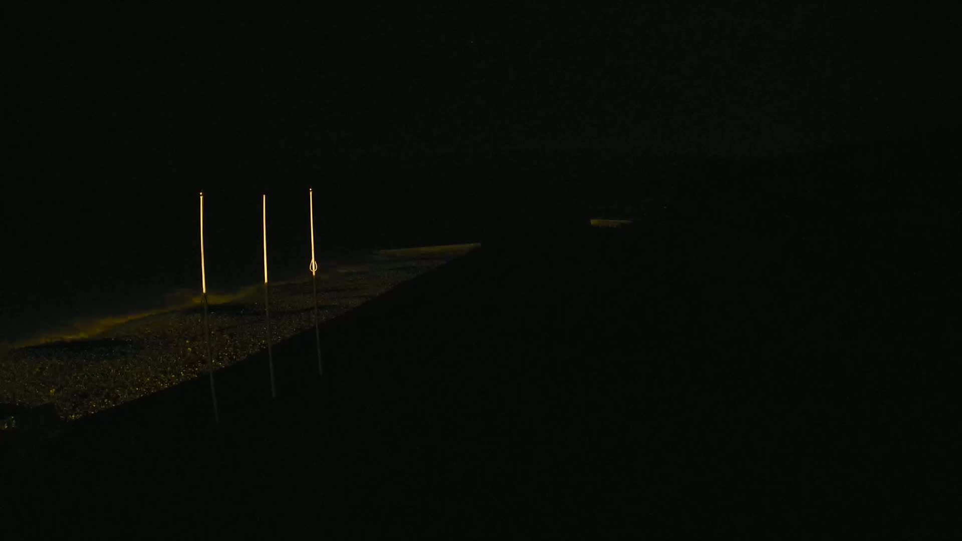 Three tall, thin lights illuminate a dark, seemingly watery surface at night.