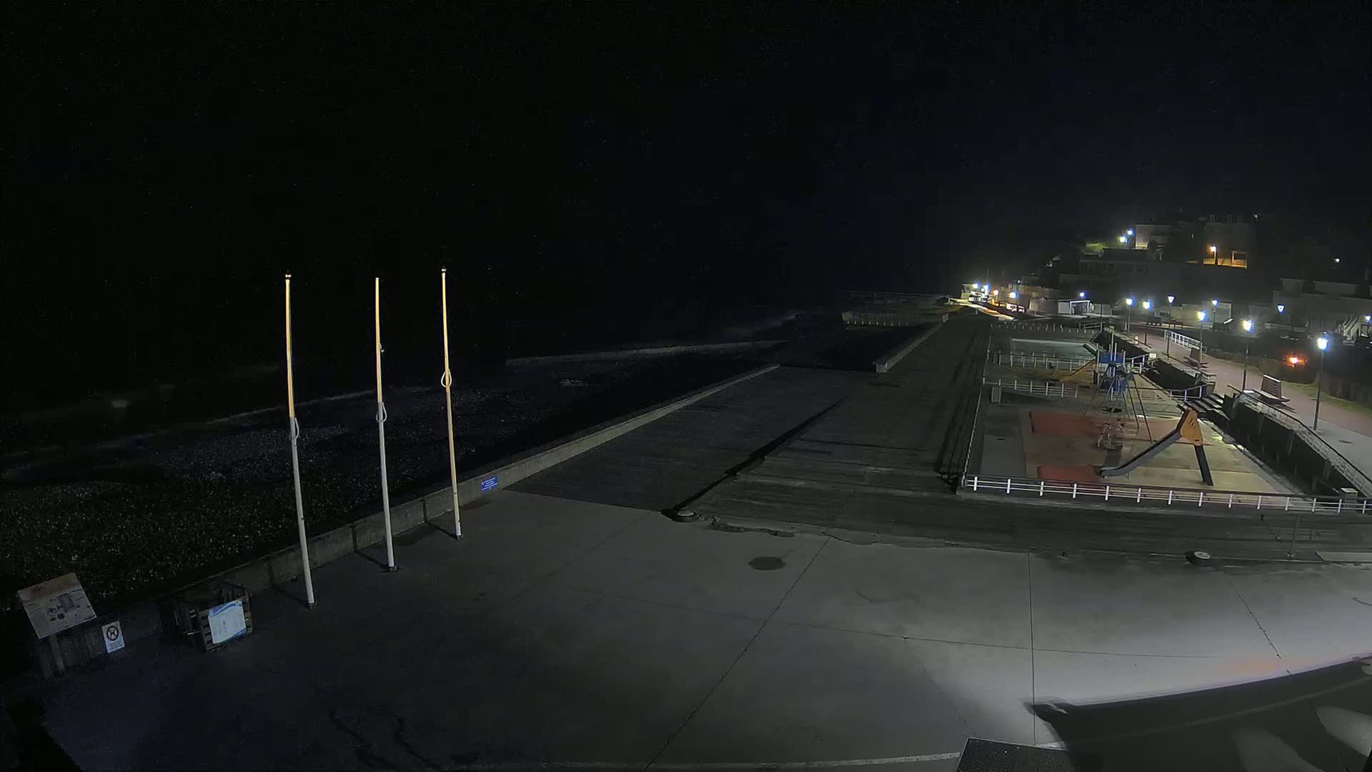 A nighttime view of a dark, empty beach with a playground and buildings lit up in the background.