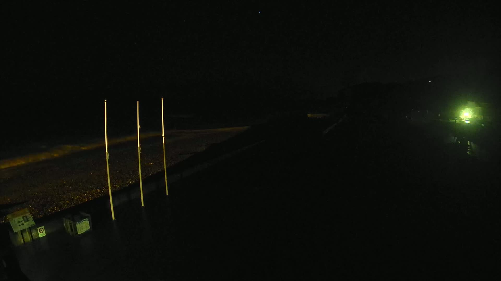 Three tall, slender poles stand on a dark, pebble-strewn beach at night under a clear, starlit sky.
